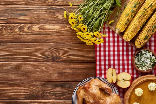 Vue du dessus de tarte à la citrouille, dinde rôtie et maïs servi à table en bois près de fleurs jaunes pour le dîner de Thanksgiving — Photo de stock