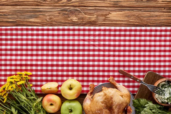 Top view of roasted turkey and apples served on red checkered napkin at wooden table for Thanksgiving dinner — Stock Photo
