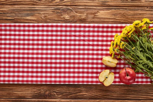 Top view of yellow wildflowers and apples on red checkered napkin at wooden table — Stock Photo
