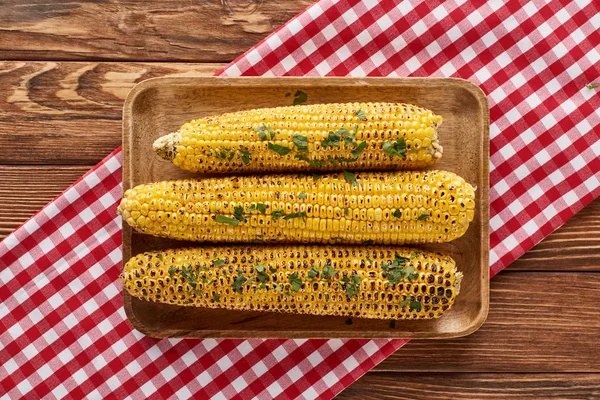 Top view of grilled corn served on red checkered napkin at wooden table for Thanksgiving dinner — Stock Photo