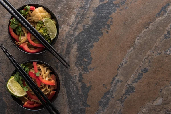 Вид сверху на вкусную пряную тайскую лапшу с палочками для еды на каменной поверхности — стоковое фото