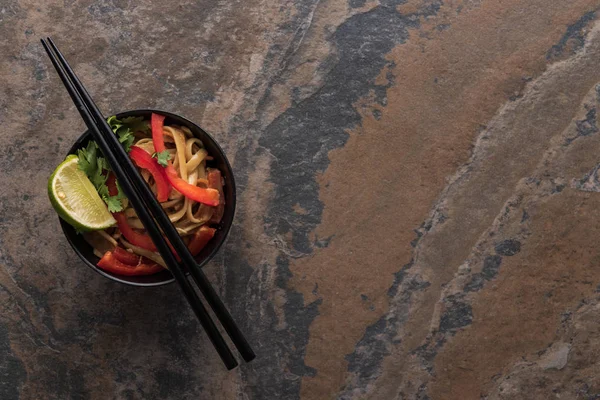 Vista superior de deliciosos fideos tailandeses picantes en un tazón con palillos en la superficie de piedra - foto de stock
