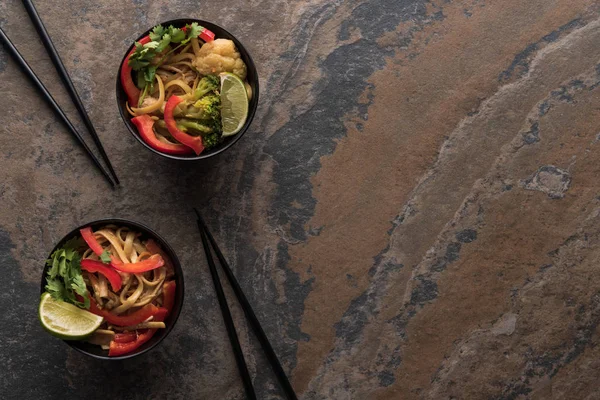 Vue de dessus des nouilles thai épicées savoureuses avec des baguettes sur la surface de la pierre — Photo de stock