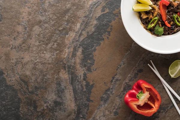 Vista dall'alto di gustose tagliatelle thai piccanti con bacchette, lime, peperone su superficie di pietra — Foto stock