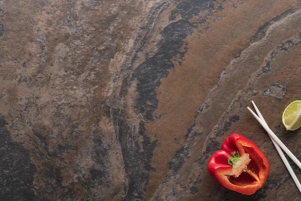 Blick von oben auf Paprika, Limette, Essstäbchen auf Steinoberfläche — Stockfoto