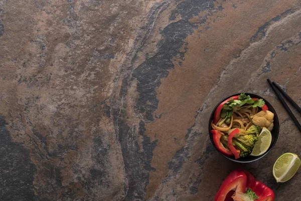 Vue de dessus des nouilles thai épicées savoureuses avec des baguettes sur la surface de la pierre — Photo de stock