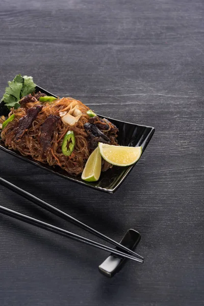 Мясо вкусная пряная тайская лапша рядом с палочками для еды на деревянной серой поверхности — стоковое фото