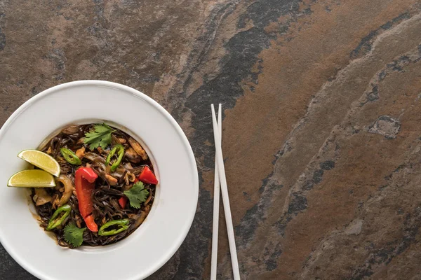 Vista superior de macarrão tailandês picante saboroso com carne e pauzinhos na superfície de pedra — Fotografia de Stock