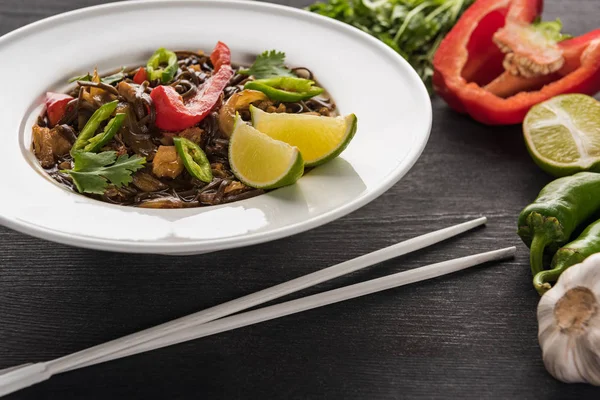 Vegetable delicious spicy thai noodles near chopsticks and ingredients on wooden grey surface — Stock Photo