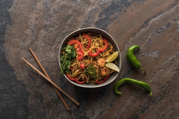 Vue de dessus des nouilles thai épicées savoureuses avec des crevettes près des baguettes sur la surface de la pierre — Photo de stock