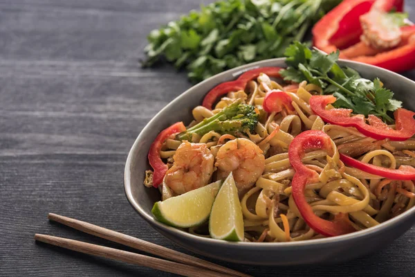 Delicious spicy thai noodles with shrimps near chopsticks on wooden grey surface — Stock Photo