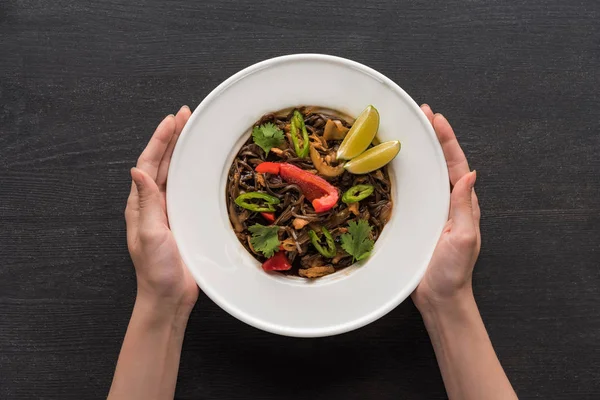 Cropped view of woman holding plate with tasty spicy thai noodles on wooden grey surface — Stock Photo