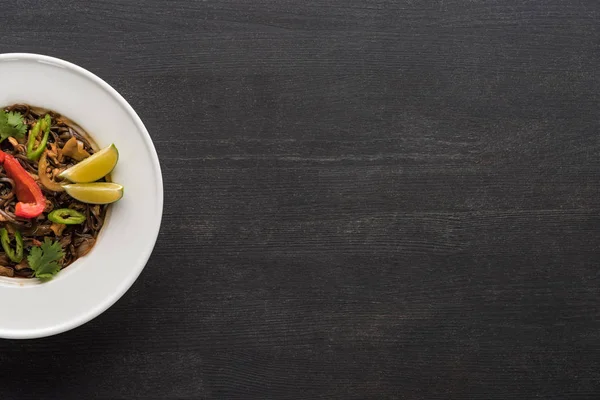 Vue de dessus des nouilles thai épicées savoureuses dans l'assiette sur la surface gris bois — Photo de stock