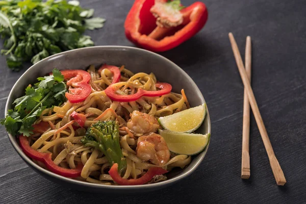 Tasty spicy thai noodles with shrimps near chopsticks on wooden grey surface — Stock Photo
