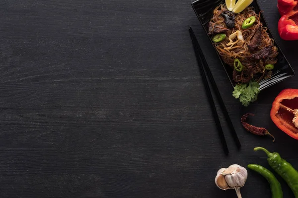 Вид зверху смачної гострої тайської локшини біля паличок та інгредієнтів на дерев'яній сірій поверхні — стокове фото