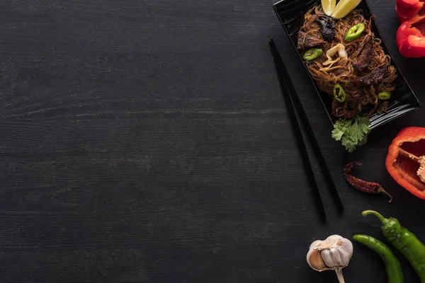 Vista dall'alto di gustose tagliatelle thai piccanti vicino a bacchette e ingredienti sulla superficie grigio legno — Foto stock