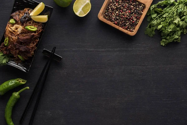 Vue de dessus des nouilles thai épicées savoureuses près des baguettes et des ingrédients frais sur la surface gris bois — Photo de stock