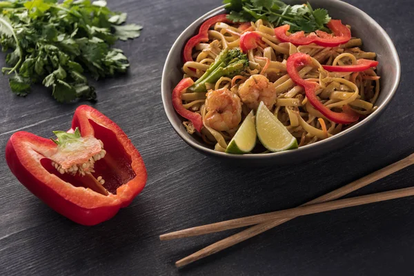 Selective focus of tasty spicy seafood thai noodles near chopsticks, paprika and parsley on wooden grey surface — Stock Photo
