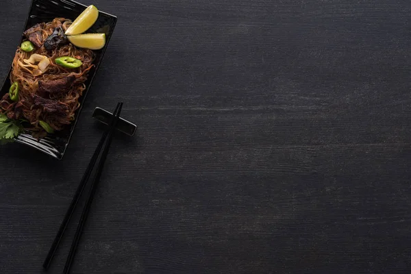 Vue de dessus des nouilles thai épicées savoureuses près des baguettes sur la surface gris bois — Photo de stock