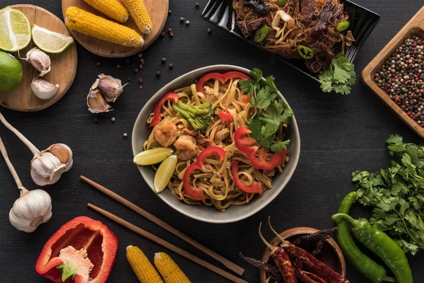 Top view of tasty spicy seafood thai noodles near chopsticks and fresh ingredients on wooden grey surface — Stock Photo