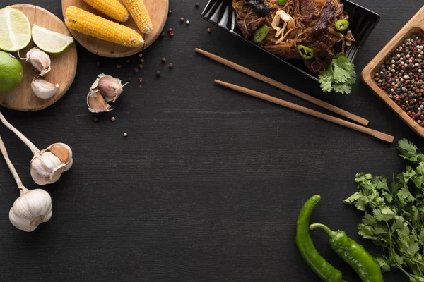 Top view of tasty spicy meat thai noodles near chopsticks and fresh ingredients on wooden grey surface with copy space — Stock Photo