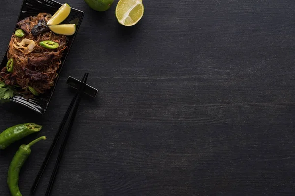 Vista superior de sabrosos fideos tailandeses de carne picante cerca de palillos en la superficie gris de madera con espacio para copiar — Stock Photo