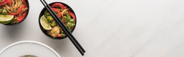 Vue de dessus de délicieuses nouilles thaï à la viande et aux légumes avec baguettes sur une surface gris marbre, vue panoramique — Photo de stock