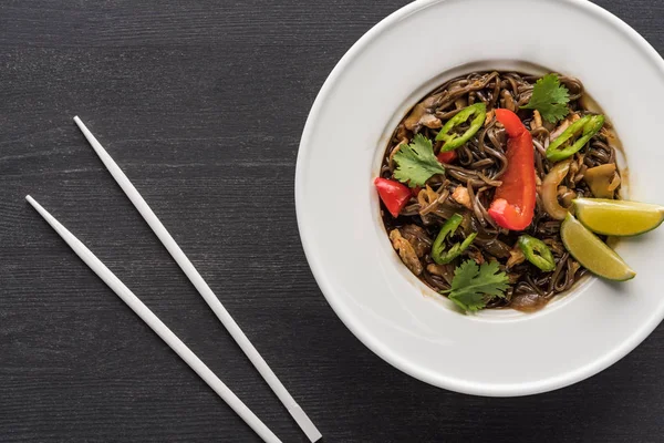 Vista dall'alto di deliziosi tagliatelle thai piccanti e bacchette bianche su tavolo grigio in legno — Foto stock