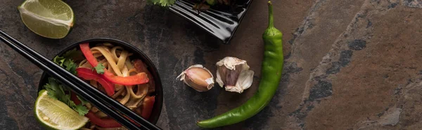 Vue de dessus de délicieuses nouilles thaï avec baguettes, ail, jalapenos et citron vert sur la surface de la pierre, vue panoramique — Photo de stock