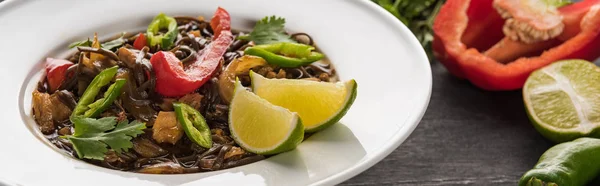 Vista de cerca de la carne fideos tailandeses cerca de los ingredientes en la superficie gris de madera, plano panorámico - foto de stock