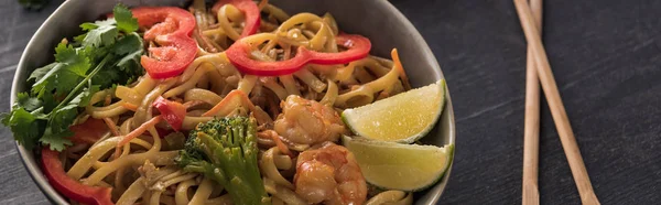 Close up view of thai noodles with shrimps near chopsticks on wooden grey surface, panoramic shot — Stock Photo