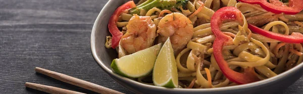 Close up view of thai noodles with shrimps near chopsticks on wooden grey surface, panoramic shot — Stock Photo