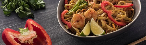 Vue rapprochée des nouilles thaïlandaises aux crevettes près du persil et du poivron sur une surface gris bois, plan panoramique — Photo de stock