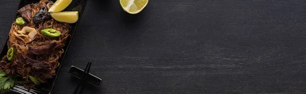 Top view of meat thai noodles near chopsticks and lime on wooden grey surface, panoramic shot — Stock Photo