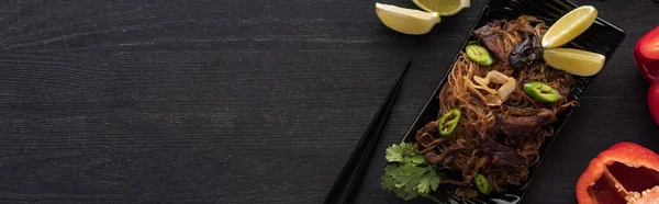 Top view of meat thai noodles near chopsticks, lime and paprika on wooden grey surface, panoramic shot — Stock Photo