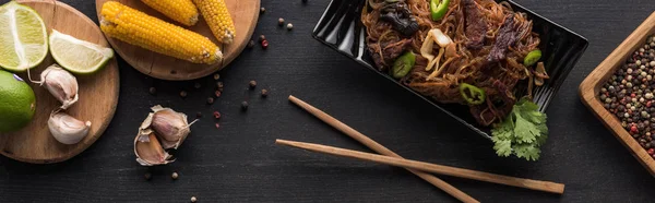 Top view of noodles near chopsticks, garlic and corn on wooden grey surface, panoramic shot — Stock Photo