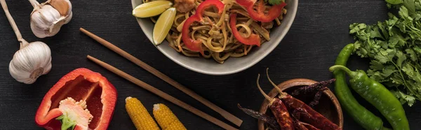 Top view of tasty spicy thai noodles with garlic, parsley, corn, bell pepper, jalapenos near chopsticks on wooden grey surface, panoramic shot — Stock Photo