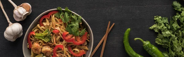 Vista dall'alto di gustosi tagliatelle thai piccanti con aglio, prezzemolo, jalapenos vicino bacchette su superficie grigio legno, colpo panoramico — Foto stock