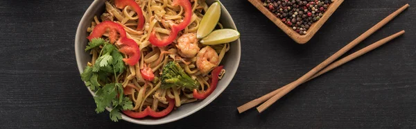 Vista dall'alto di gustose tagliatelle thai piccanti con frutti di mare vicino a bacchette su superficie grigio legno, colpo panoramico — Foto stock