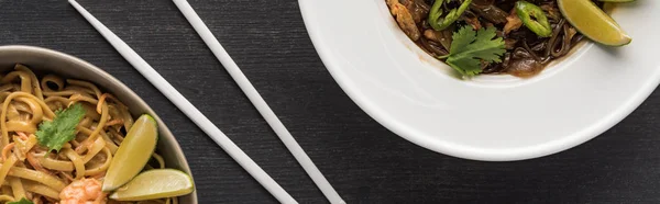 Вид сверху на вкусную пряную тайскую лапшу рядом с палочками для еды на деревянной серой поверхности, панорамный снимок — стоковое фото