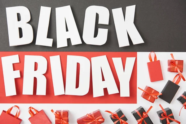 Ansicht des Black Friday Schriftzugs in der Nähe von Geschenken auf schwarzem, rotem und weißem Hintergrund — Stockfoto