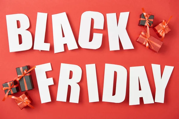 Top view of black friday white lettering near small presents on red background — Stock Photo