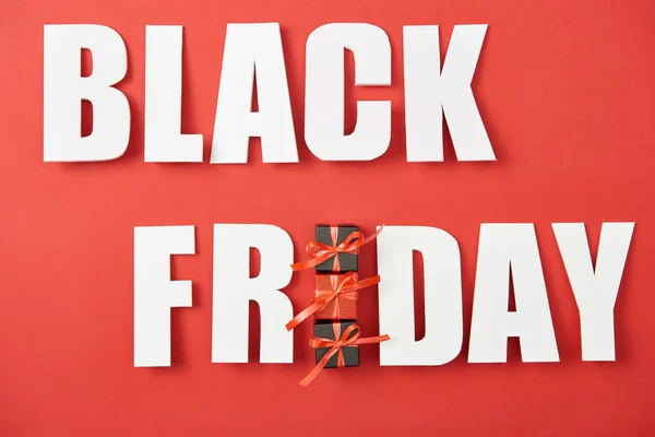 Top view of black friday white lettering with small presents on red background — Stock Photo