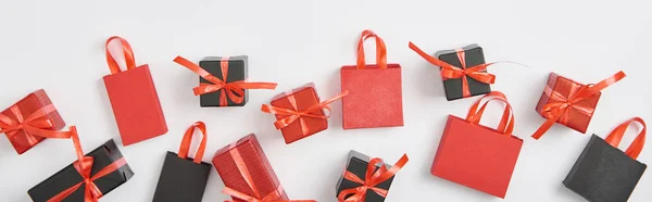 Plano panorámico de regalos negros y rojos y bolsas de compras sobre fondo blanco - foto de stock