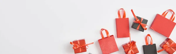 Vista dall'alto di regali neri e rossi e shopping bag su sfondo bianco con spazio copia, scatto panoramico — Foto stock
