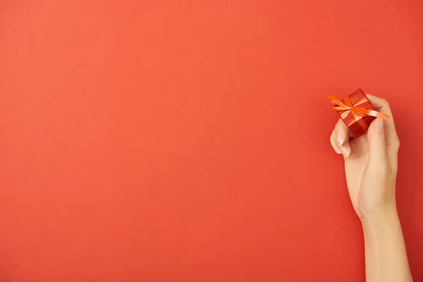 Cropped view of woman holding gift box on red background with copy space — Stock Photo