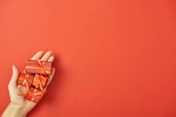 Vista parcial de la mujer sosteniendo cajas de regalo decorativas en la mano sobre fondo rojo con espacio de copia - foto de stock