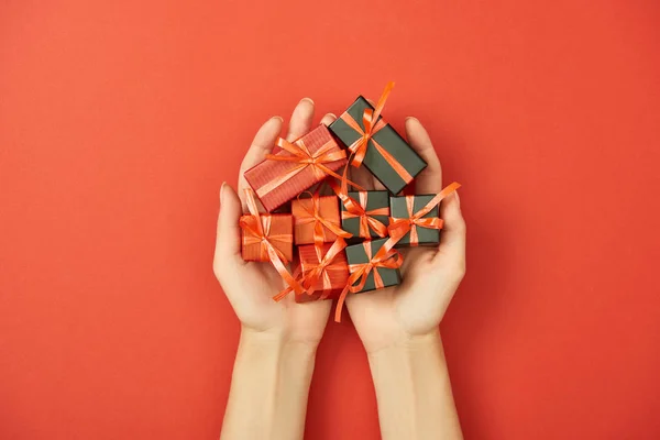 Частичный вид женщины, держащей декоративные подарочные коробки на красном фоне — стоковое фото