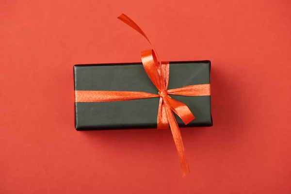 Top view of black gift box with bow and ribbon on red background — Stock Photo