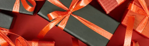 Vista dall'alto di scatole regalo con fiocchi e nastri su sfondo rosso, scatto panoramico — Foto stock